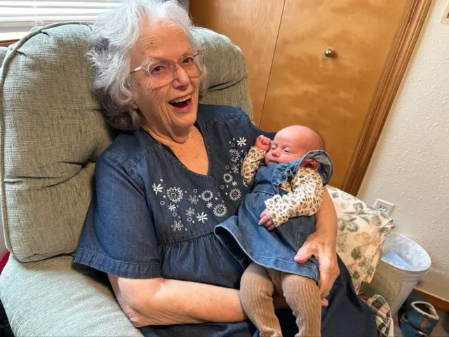 Resident holding a baby and smiling at AAA Shepherd’s Care Home