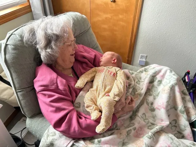 Resident holding a baby in an armchair at AAA Shepherd’s Care Home