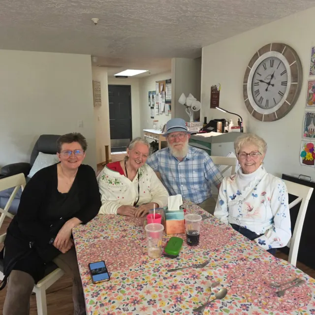 Residents and staff smiling around the dining table at AAA Shepherd’s Care Home